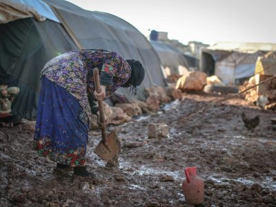 An elderly woman works in the mud at an outdoor refugee camp in Idlib, Syria.