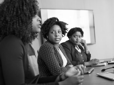 Three black women engaged in a serious discussion at an office meeting.