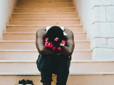 A person sits contemplatively on outdoor stairs in Mombasa, adorned with vibrant flowers.