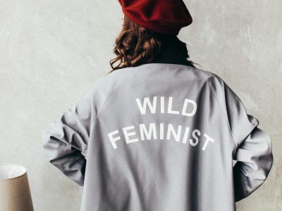 Woman in a red beret with 'Wild Feminist' coat in a cozy room setting.