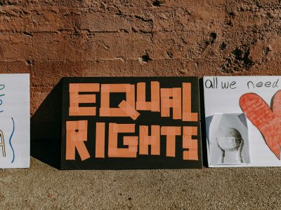 Three protest signs promoting equal rights and activism displayed on a textured wall.