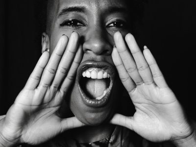 Grayscale portrait of a black woman energetically shouting, conveying strong emotions.